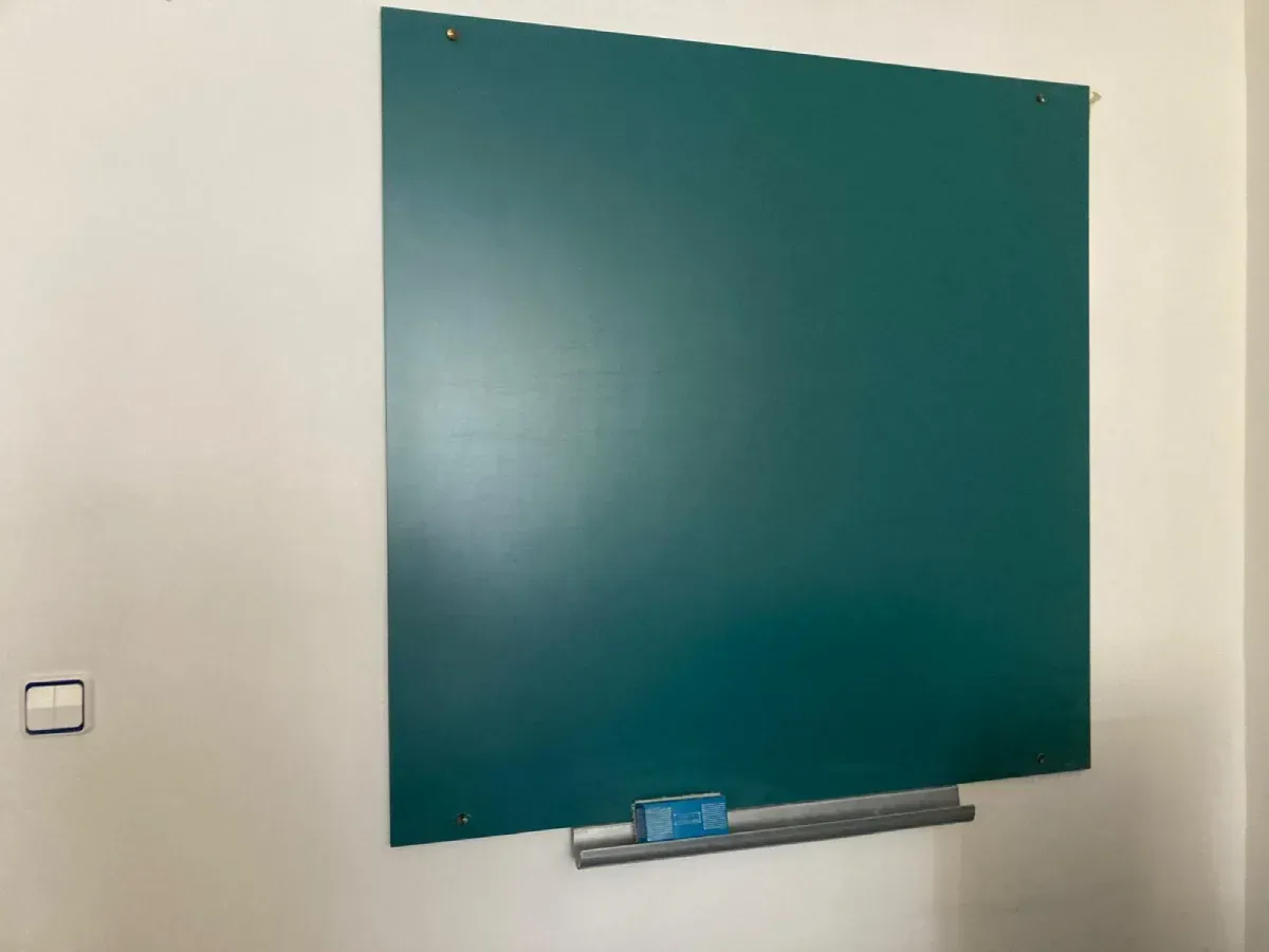 Pizarra verde montada sobre una pared blanca con una bandeja metálica adjunta que contiene un borrador y tiza.