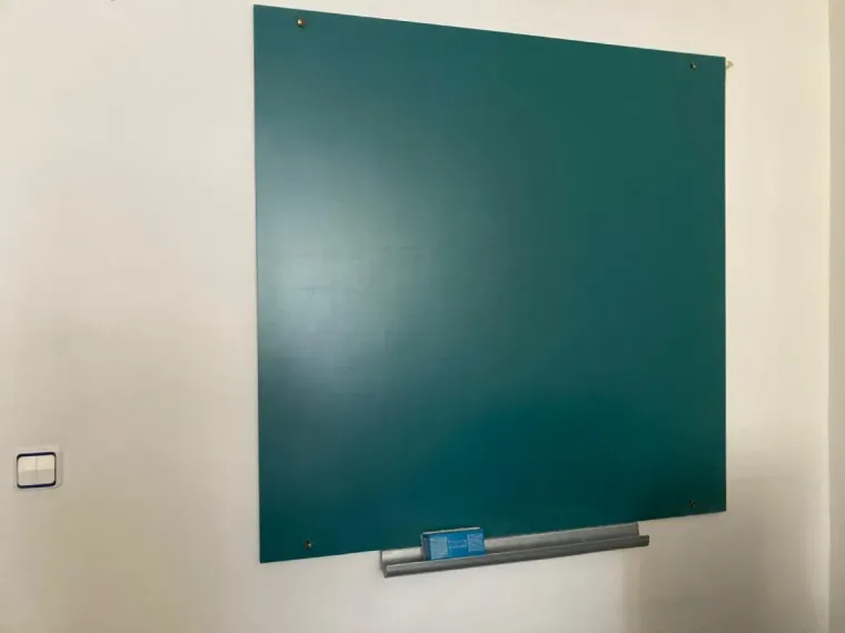 Pizarra verde montada sobre una pared blanca con una bandeja metálica adjunta que contiene un borrador y tiza.