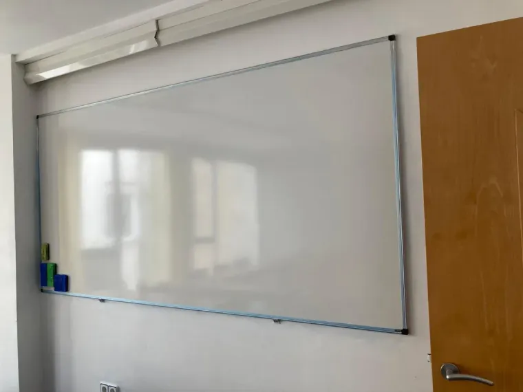 Pizarra blanca en la pared, con una puerta a la derecha y una lámpara encima.