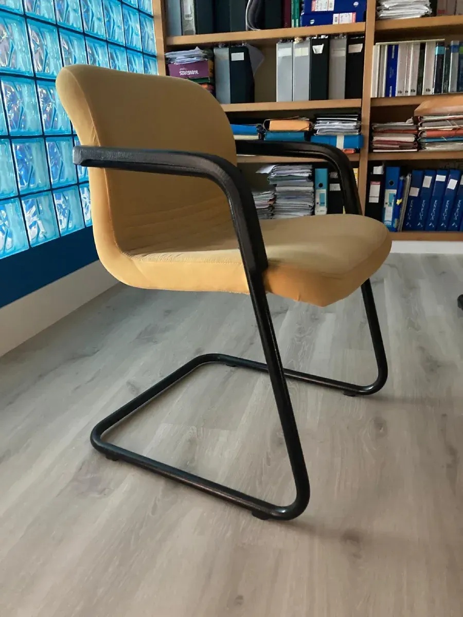 Silla de oficina tapizada en amarillo con estructura metálica negra, colocada sobre un suelo gris claro