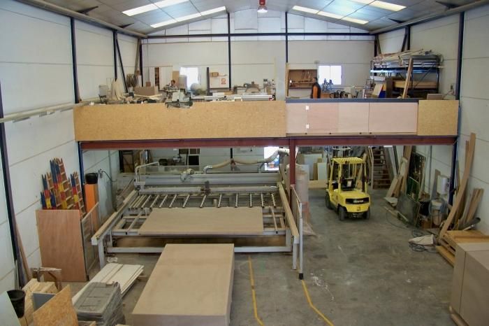 Una carretilla elevadora amarilla está moviendo una gran pieza de madera en un almacén.