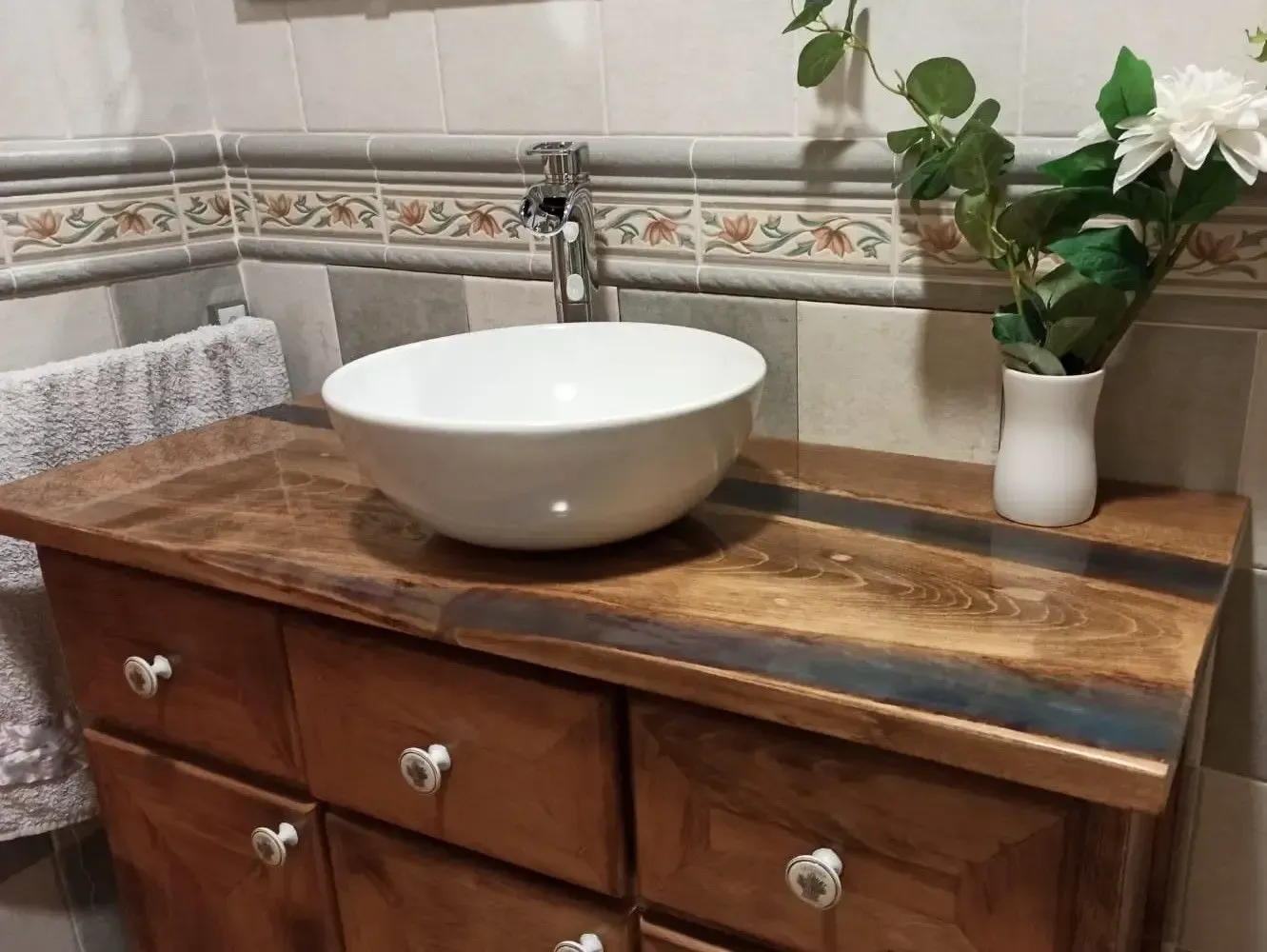 Un tocador de baño con lavabo y un jarrón de flores.