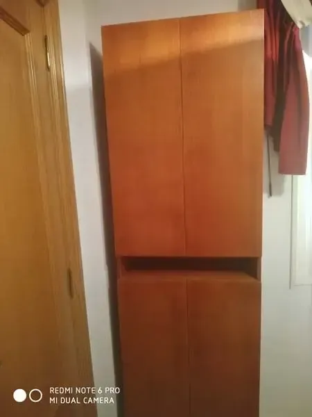Un armario de madera está en una habitación al lado de una puerta.