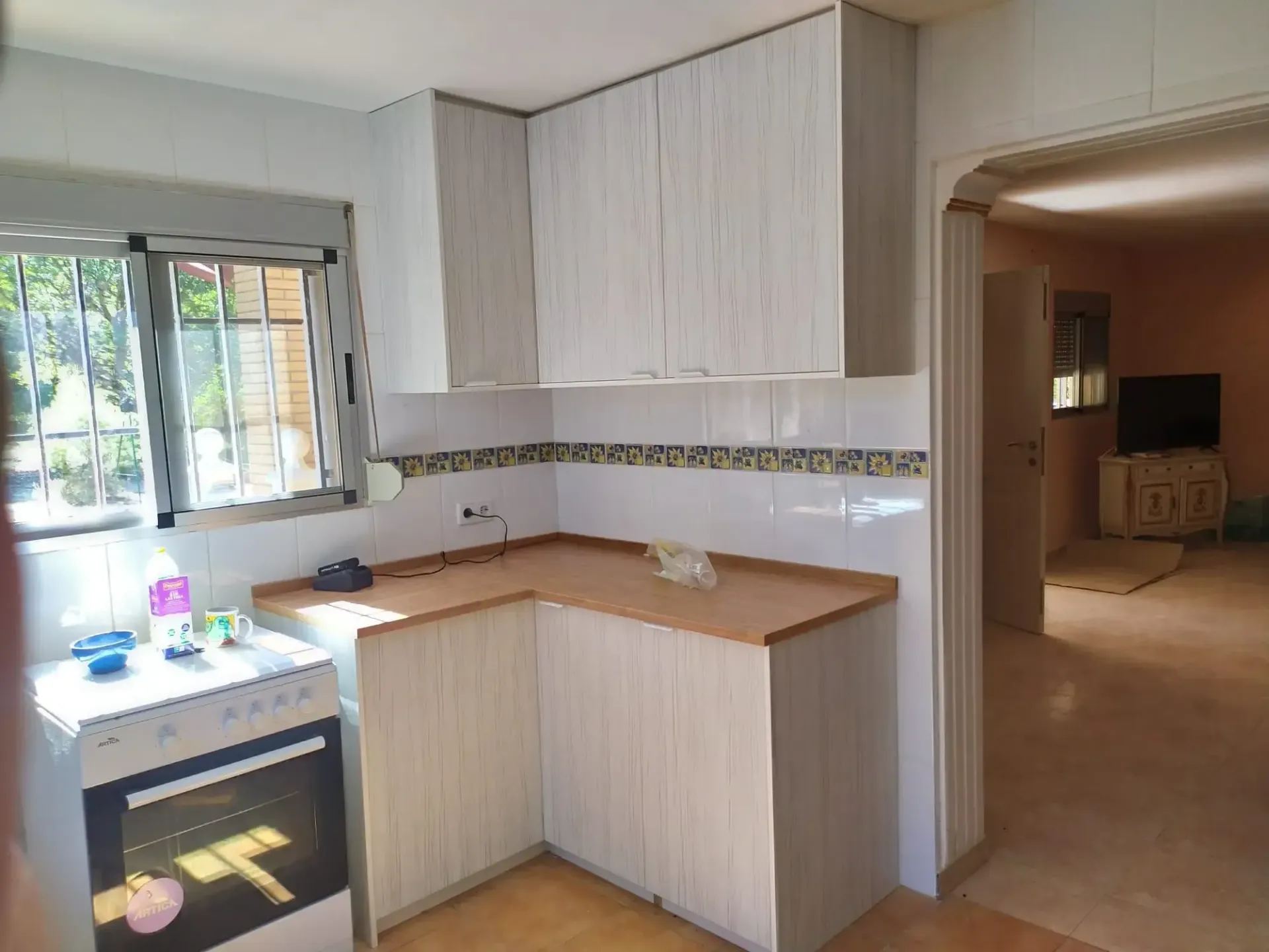 Una cocina con gabinetes blancos, una estufa y una ventana.