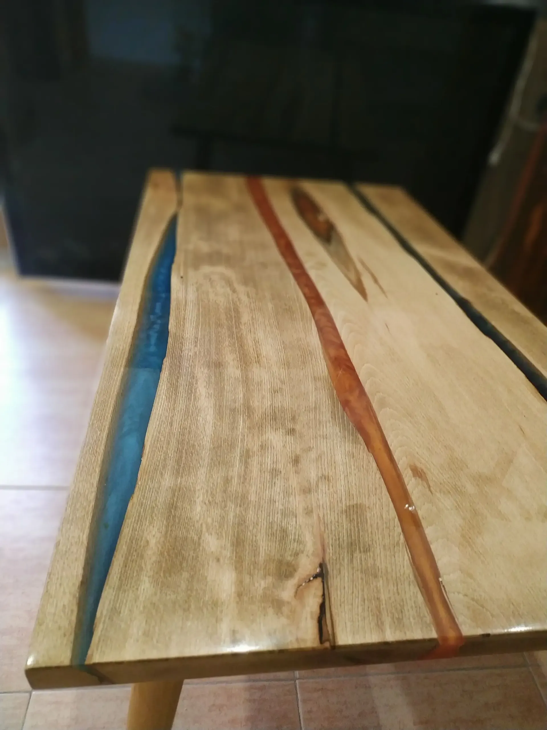 Una mesa de madera con resina azul y roja sobre ella está colocada sobre un suelo de baldosas.