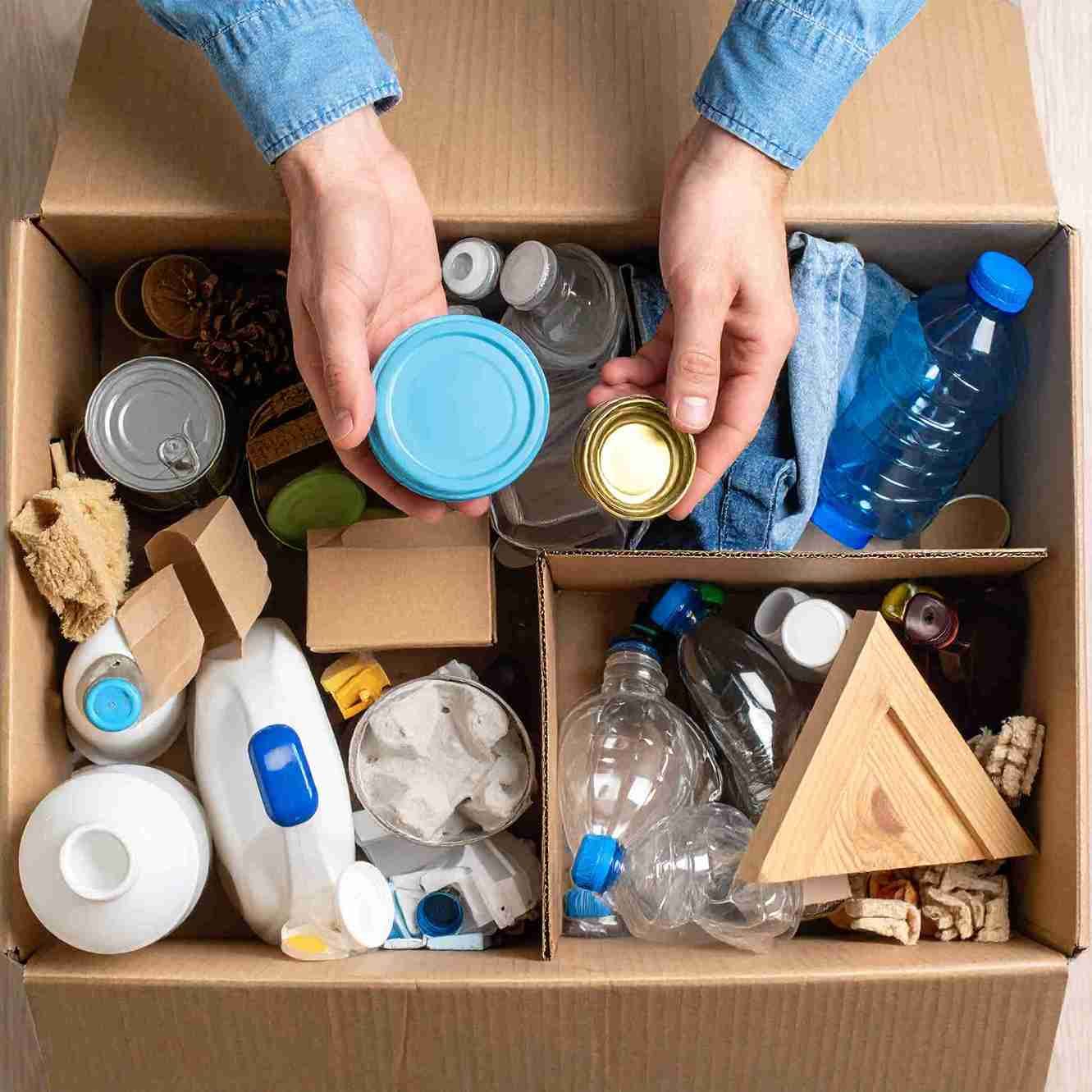 Una persona clasifica artículos reciclables en una caja de cartón.