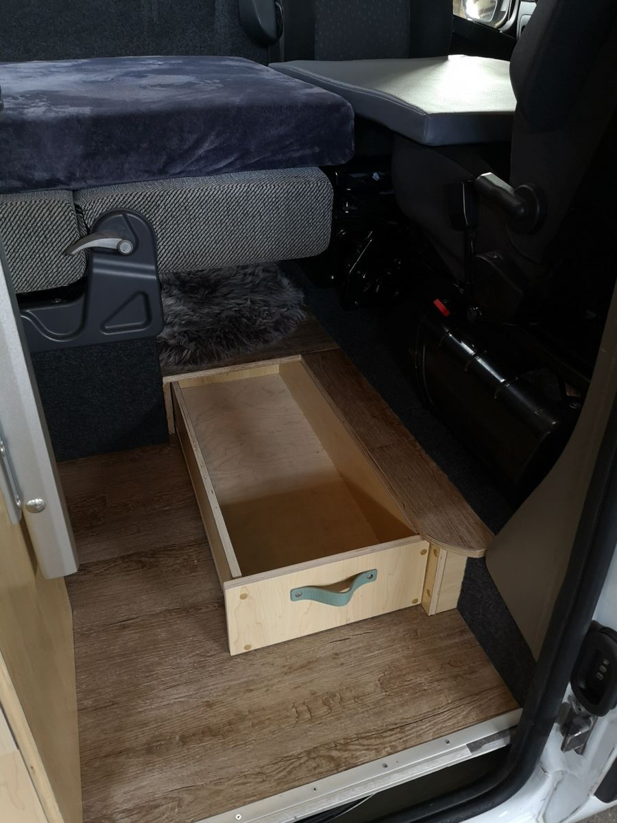 eine Holzkiste mit einem blauen Griff sitzt unter einem Bett in einem Auto
