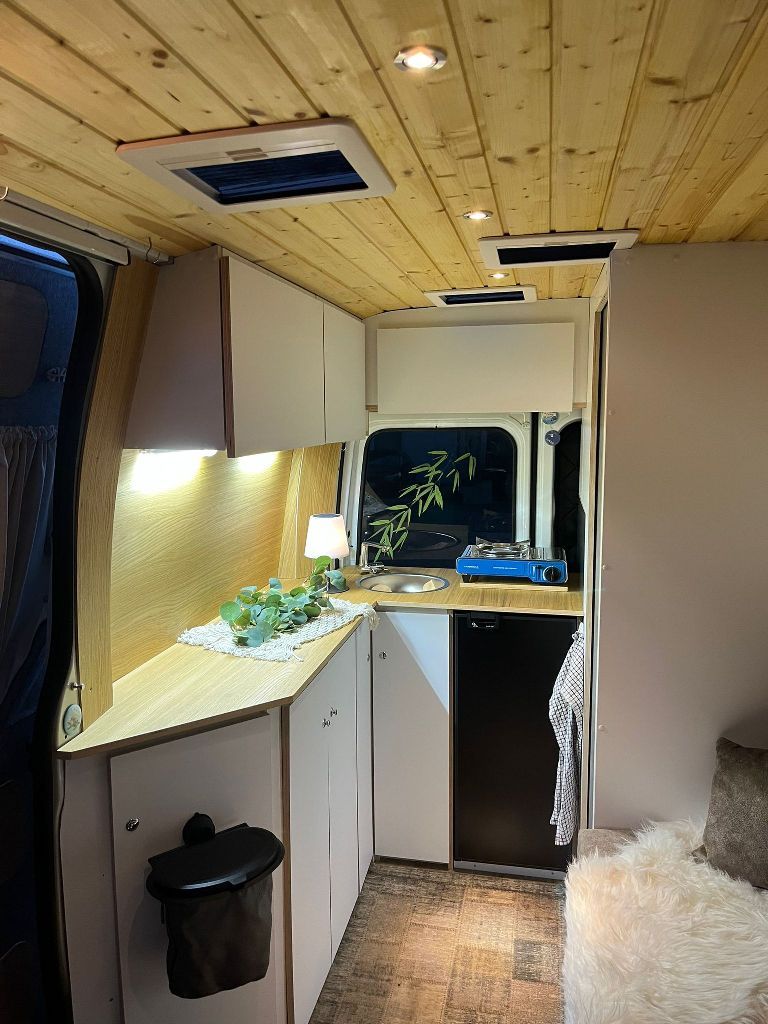 eine kleine Küche in einem Lieferwagen mit Holzdecke und weißen Schränken