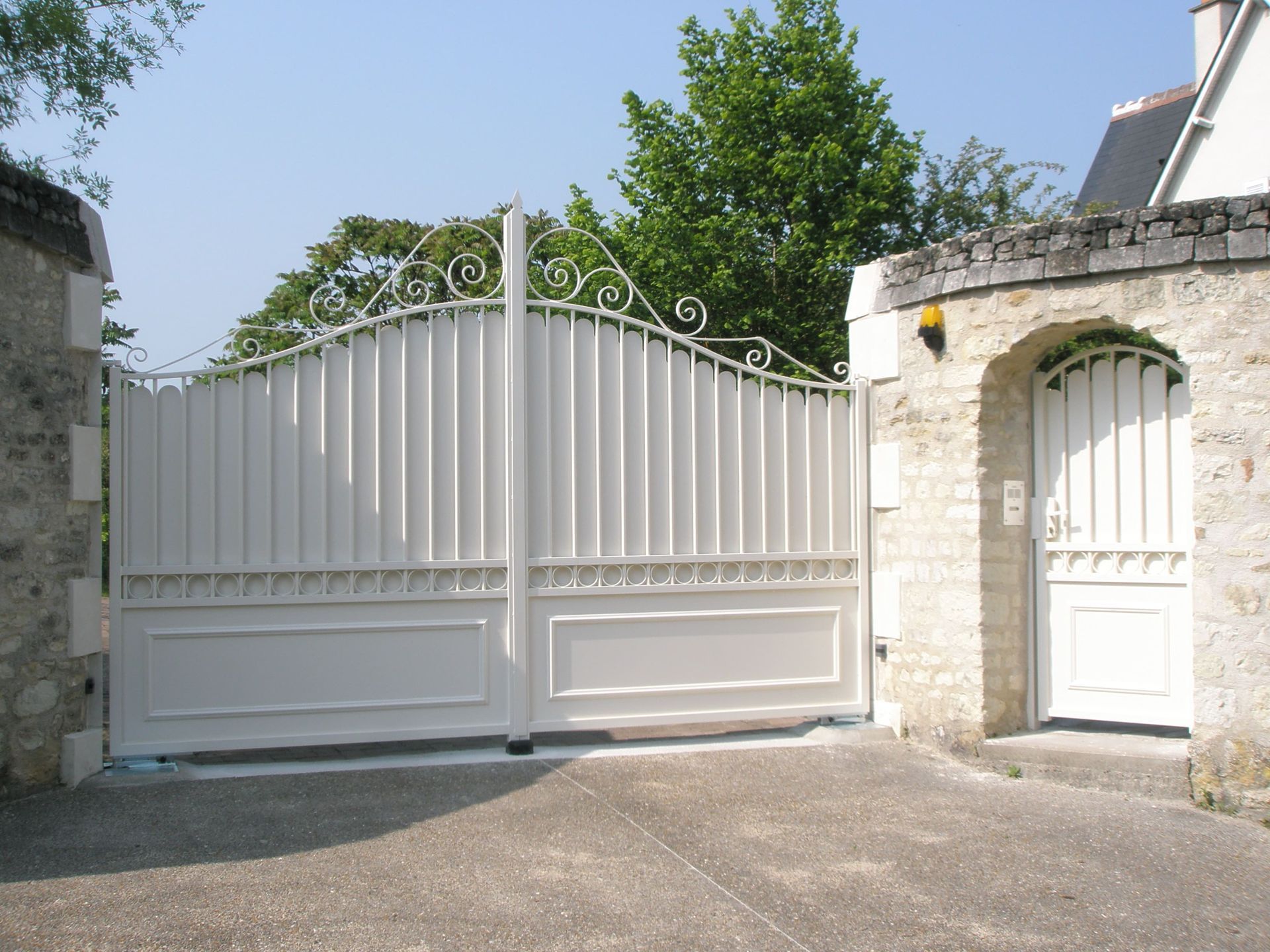 Portail en fer blanc avec un portillon à côté dans un mur en pierre