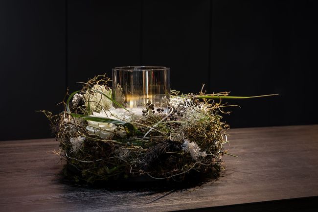 Bunte Blumenarrangements in weißen Töpfen auf pinken Stühlen und einem Tisch, umgeben von farbenfrohen Blüten in einem Gartenambiente