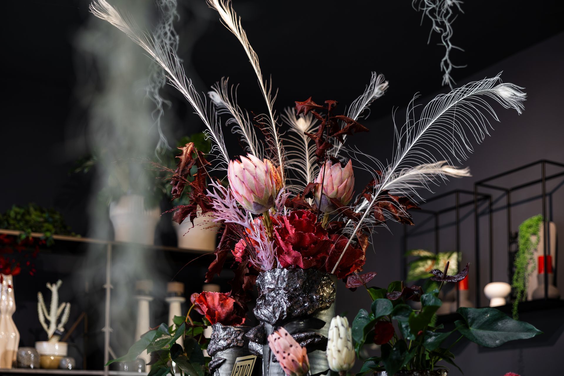 Hände, die Blumen in Vasen auf einem Tisch mit Grün und pfirsichfarbenen Blüten arrangieren
