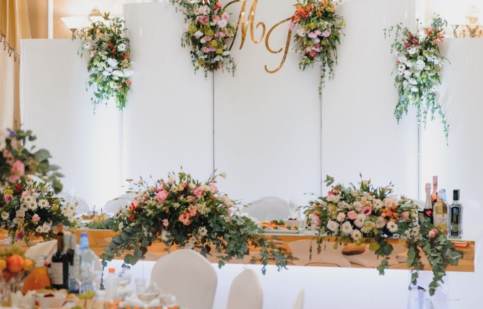 Eleganter Blumentisch für Veranstaltungen mit rosa-weißen Arrangements, Kerzen und Flaschen vor weißem Hintergrund