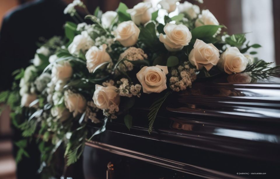 Weiße Rosen und Grünzeug auf einem dunklen Holzsarg angeordnet
