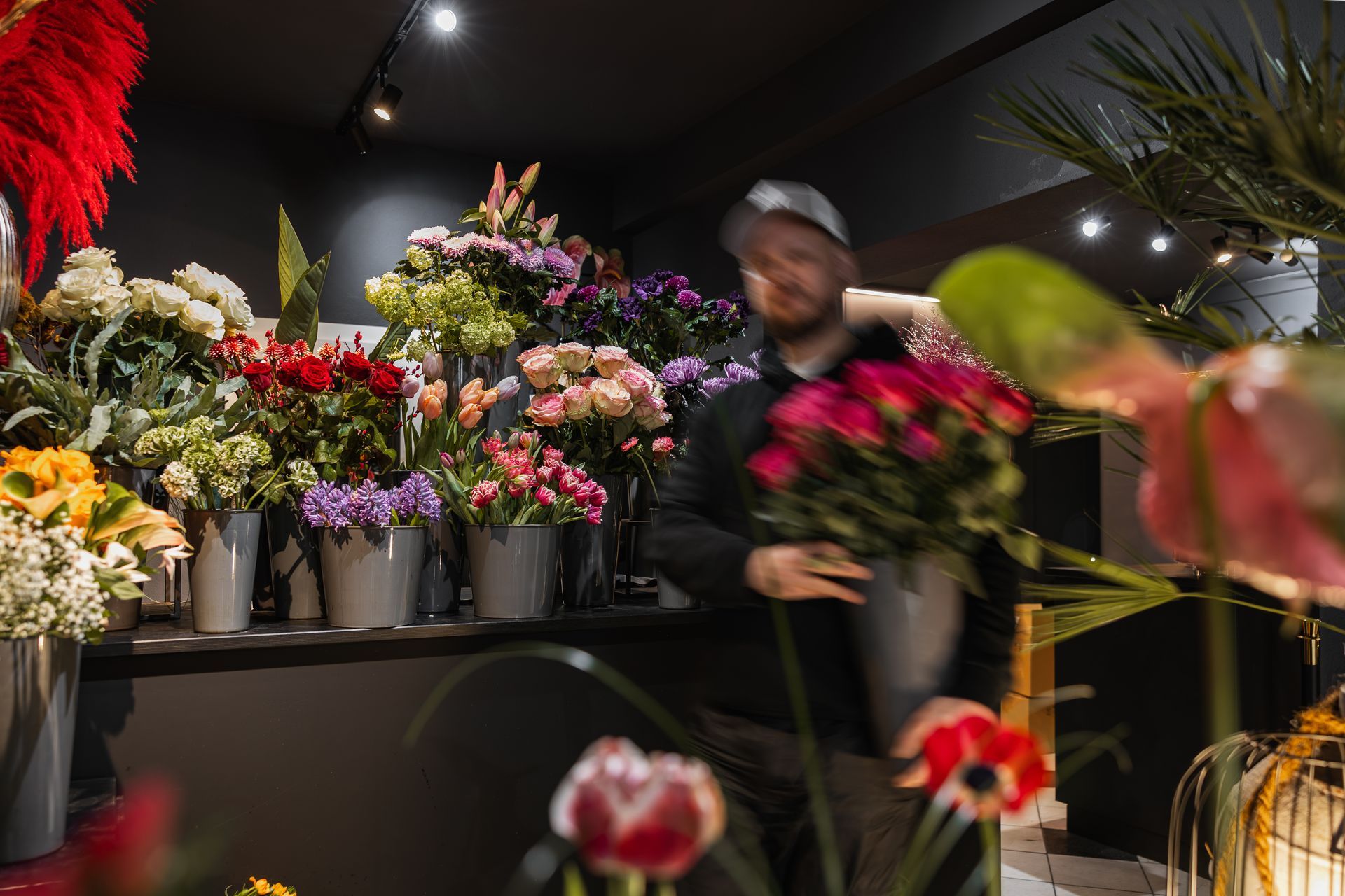 Hände, die mit einer Schere und einem rosa Band einen bunten Blumenstrauß binden