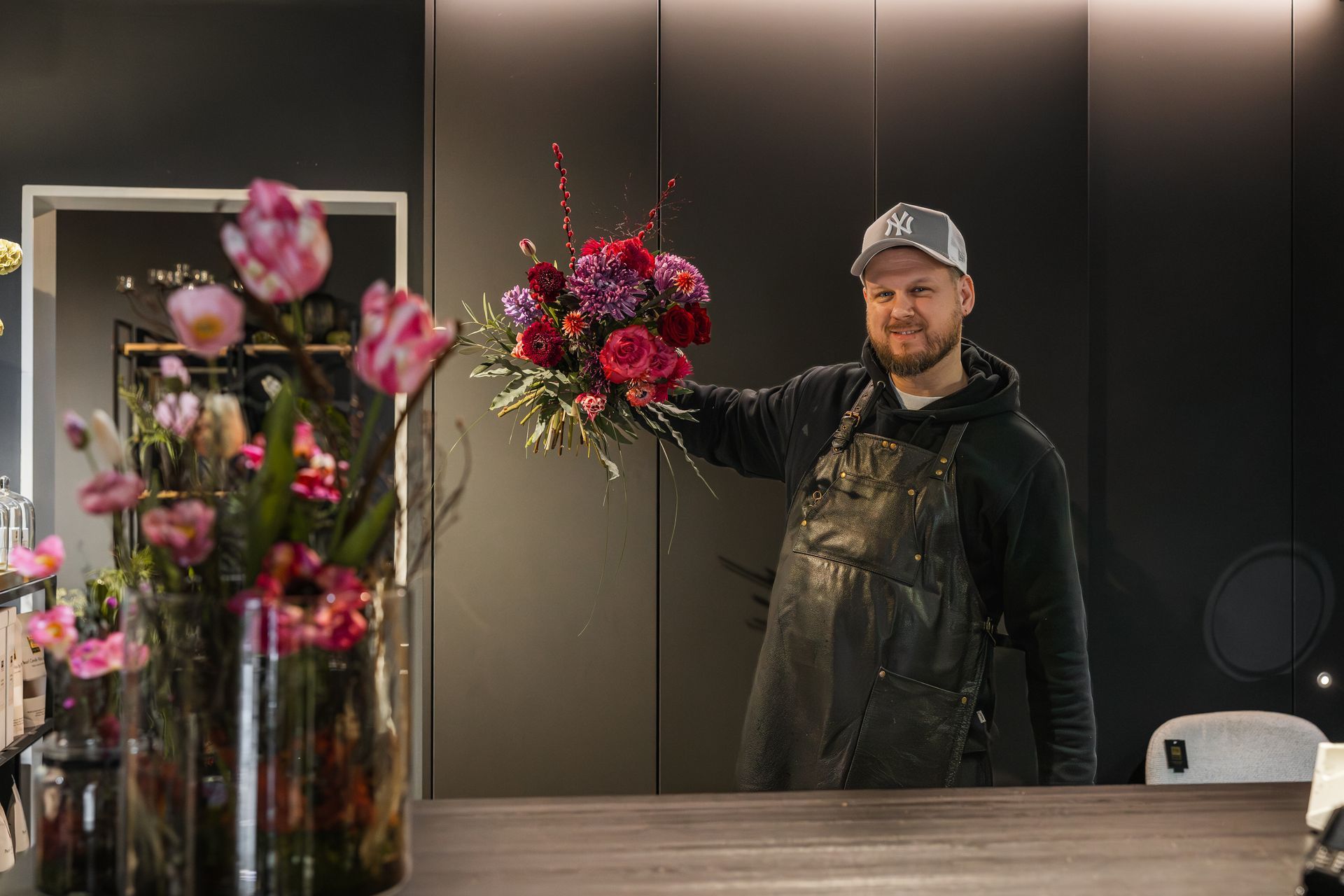 Hände, die auf einem Markt im Freien bunte Blumensträuße arrangieren, wobei rosa und pfirsichfarbene Blüten im Mittelpunkt stehen
