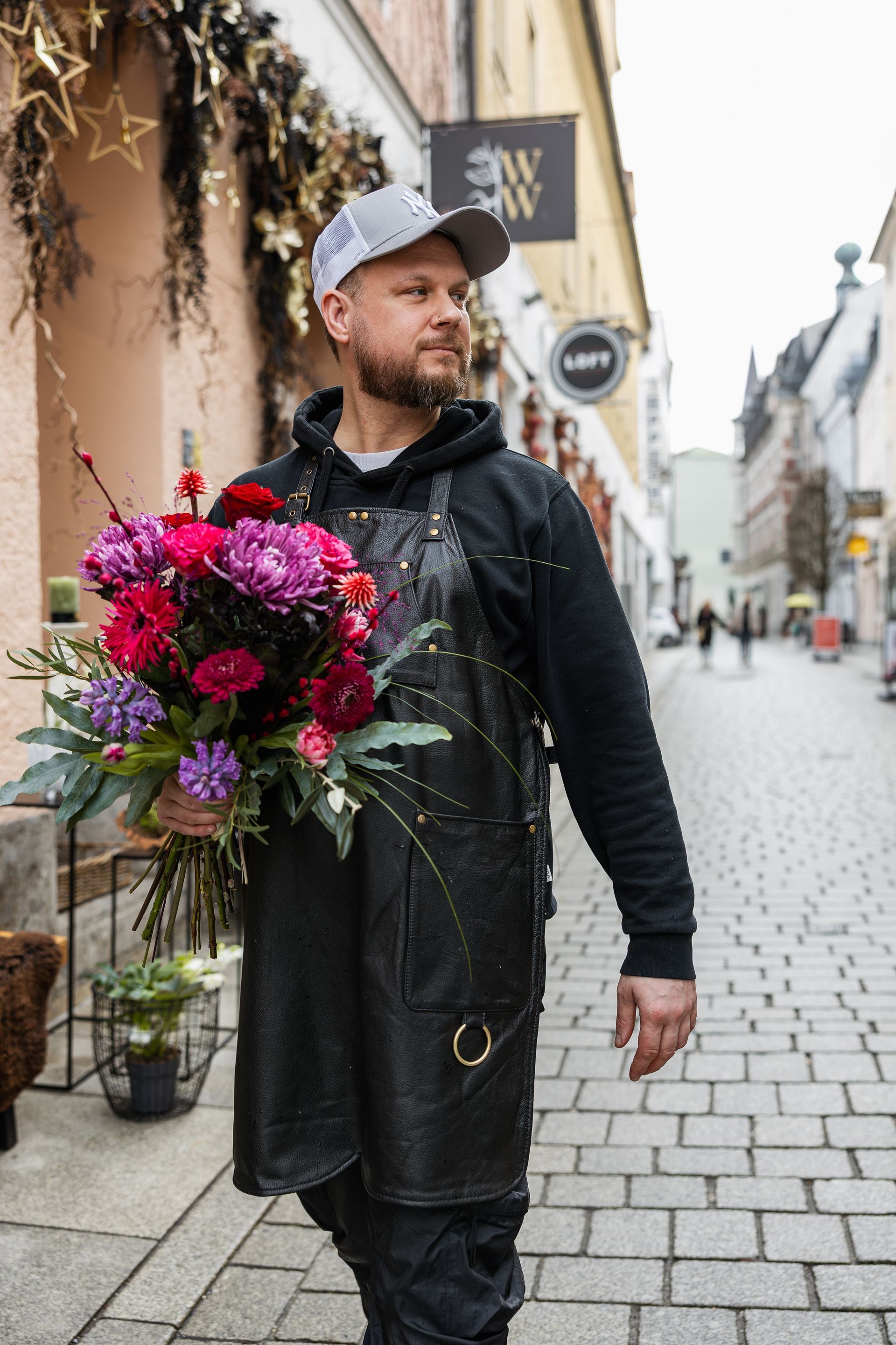 Hände arrangieren einen rosafarbenen Blumenstrauß auf einem Tisch mit verstreuten Blumen und Gartengeräten