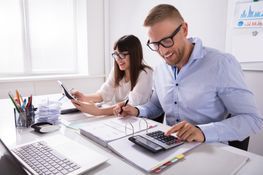 Mann und Frau berechnen mit Taschenrechner etwas mit Dokumenten und Laptop