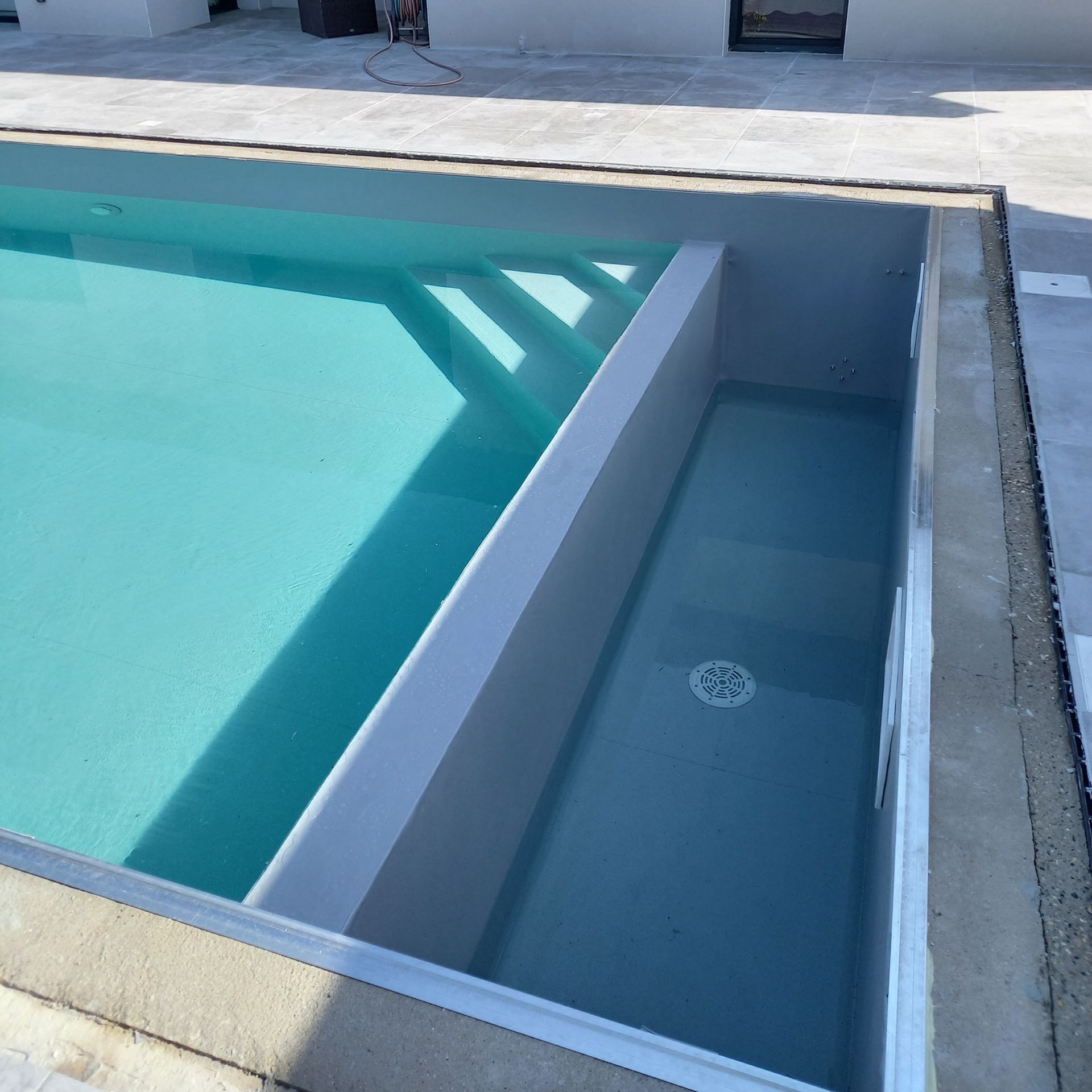 Une piscine partiellement remplie, avec une partie peu profonde, des marches et une partie plus profonde munie d'une bonde de vidange.
