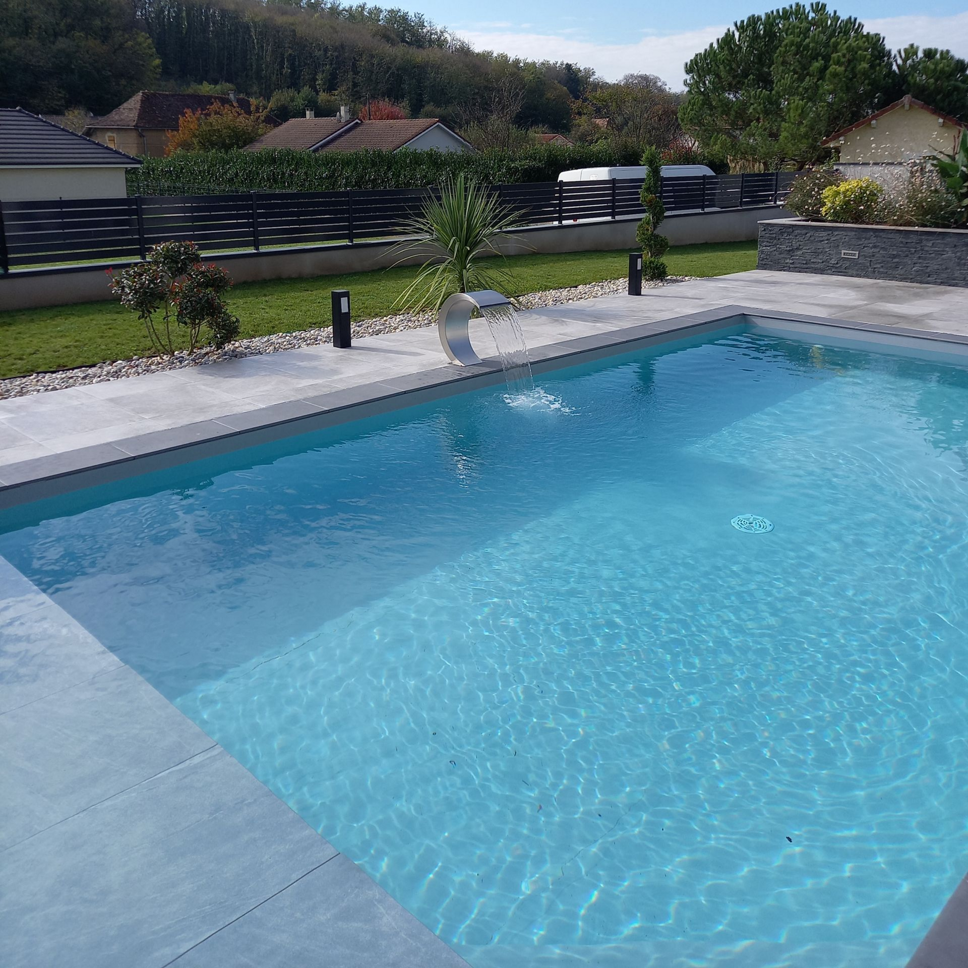 Une piscine rectangulaire d'un bleu limpide, située dans un jardin bien entretenu avec une terrasse en pierre.