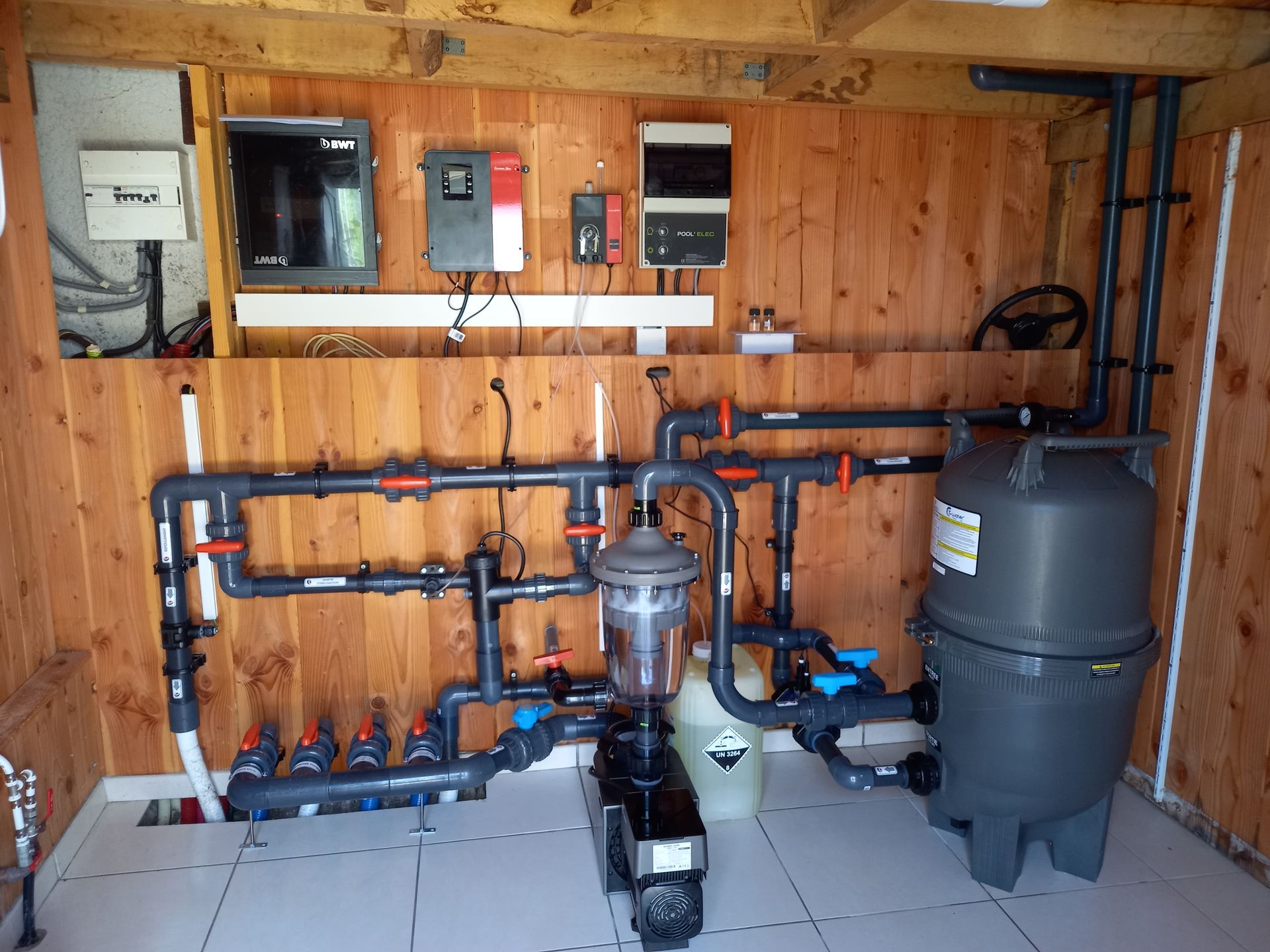 Local technique de la piscine avec plomberie, filtration et panneaux de commande.