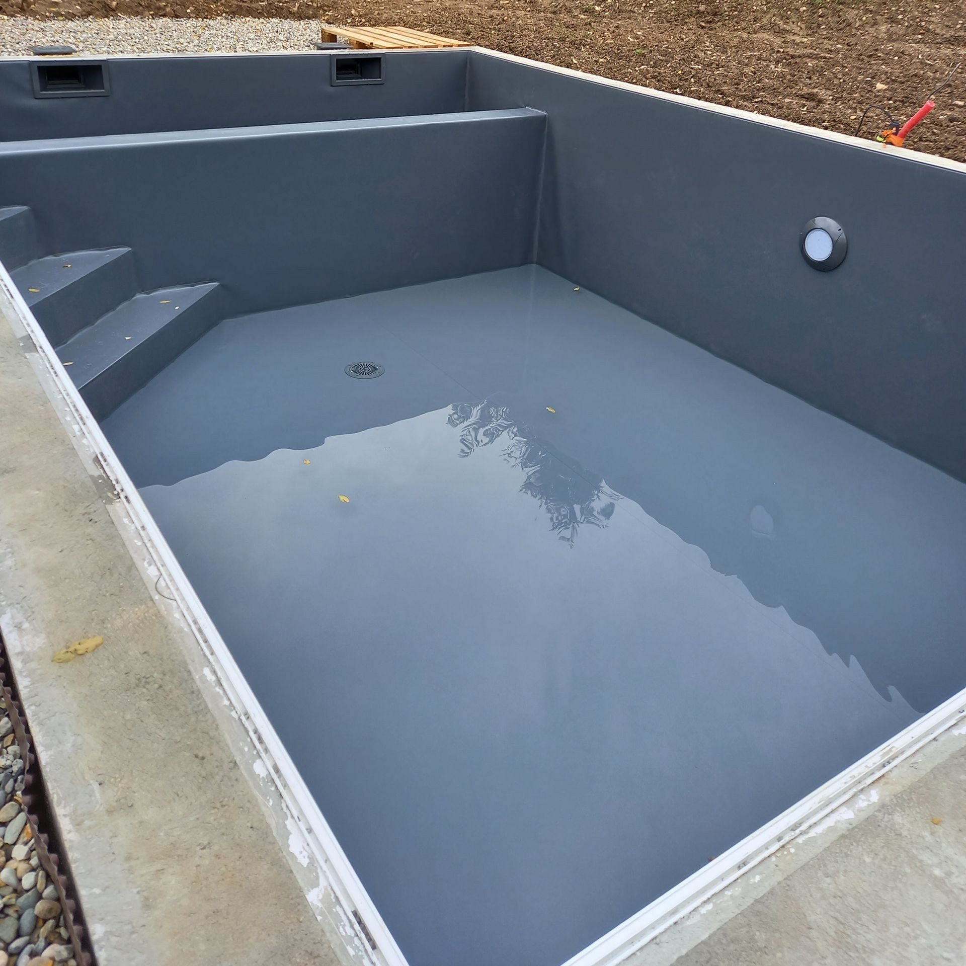 Intérieur d'une piscine rectangulaire grise avec marches, éclairage et eau. Le tout est intégré dans du béton.