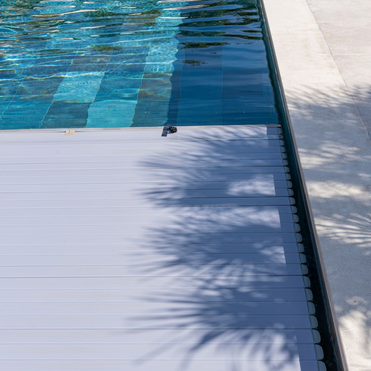 Piscine à eau bleue et couverture grise, marches visibles, avec des ombres.