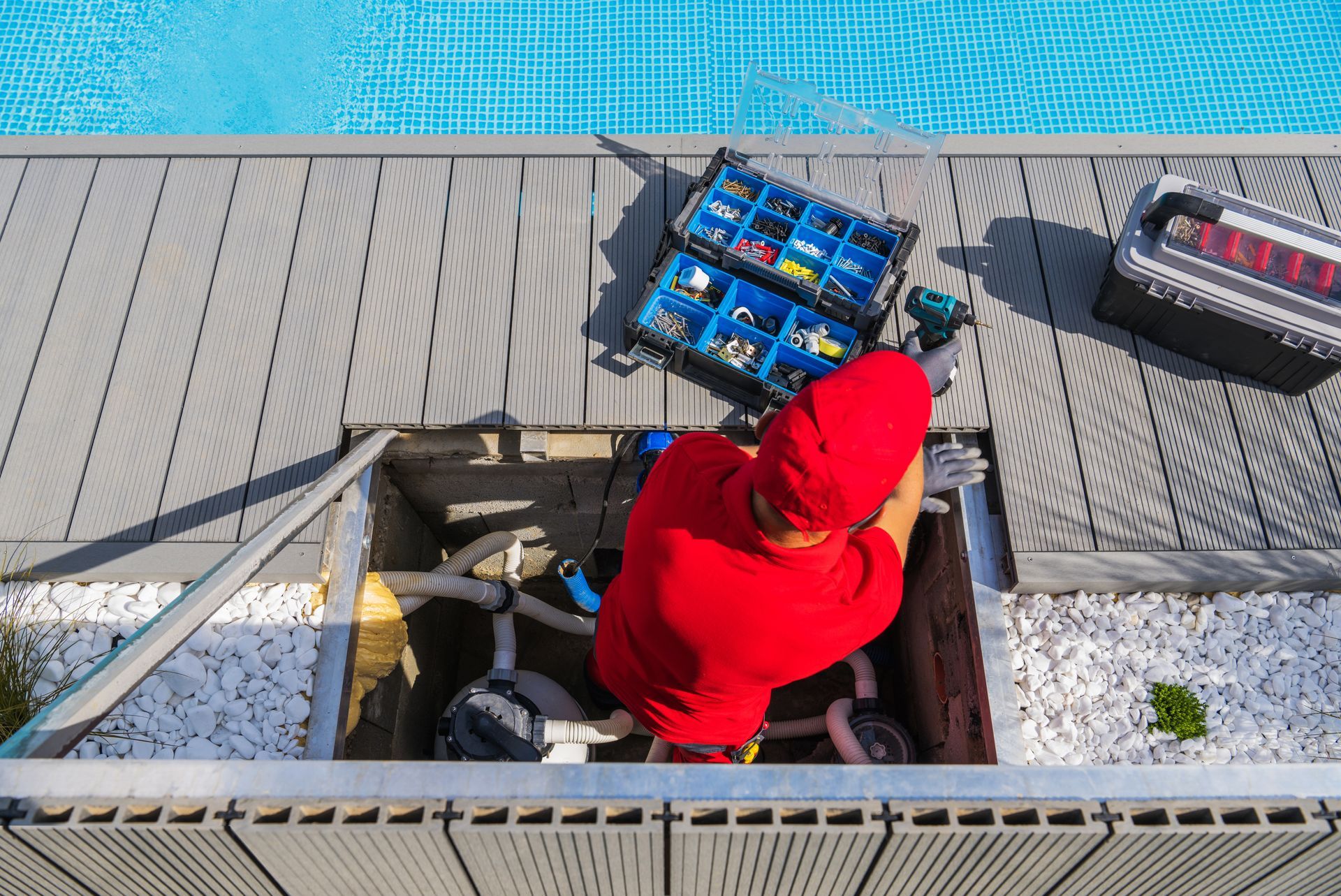 Personne en chemise rouge travaillant sur du matériel de piscine près d'une piscine, outils visibles.