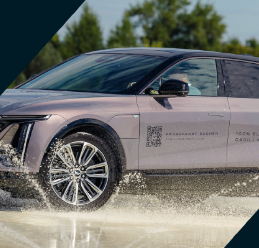 Ein silberner elektrischer SUV fährt durch flaches Wasser und spritzt dabei über eine Straße.