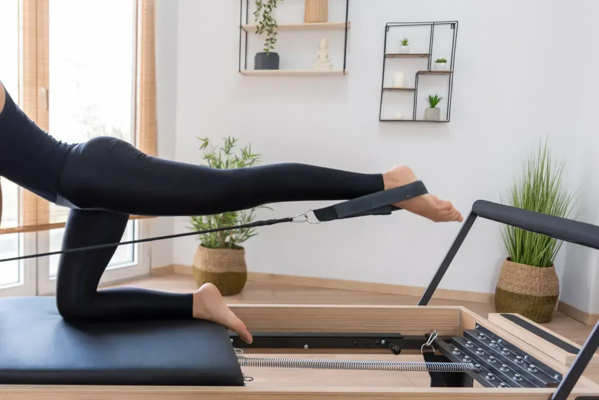Mujer haciendo ejercicio en un reformador de Pilates, con la pierna extendida, en el interior.