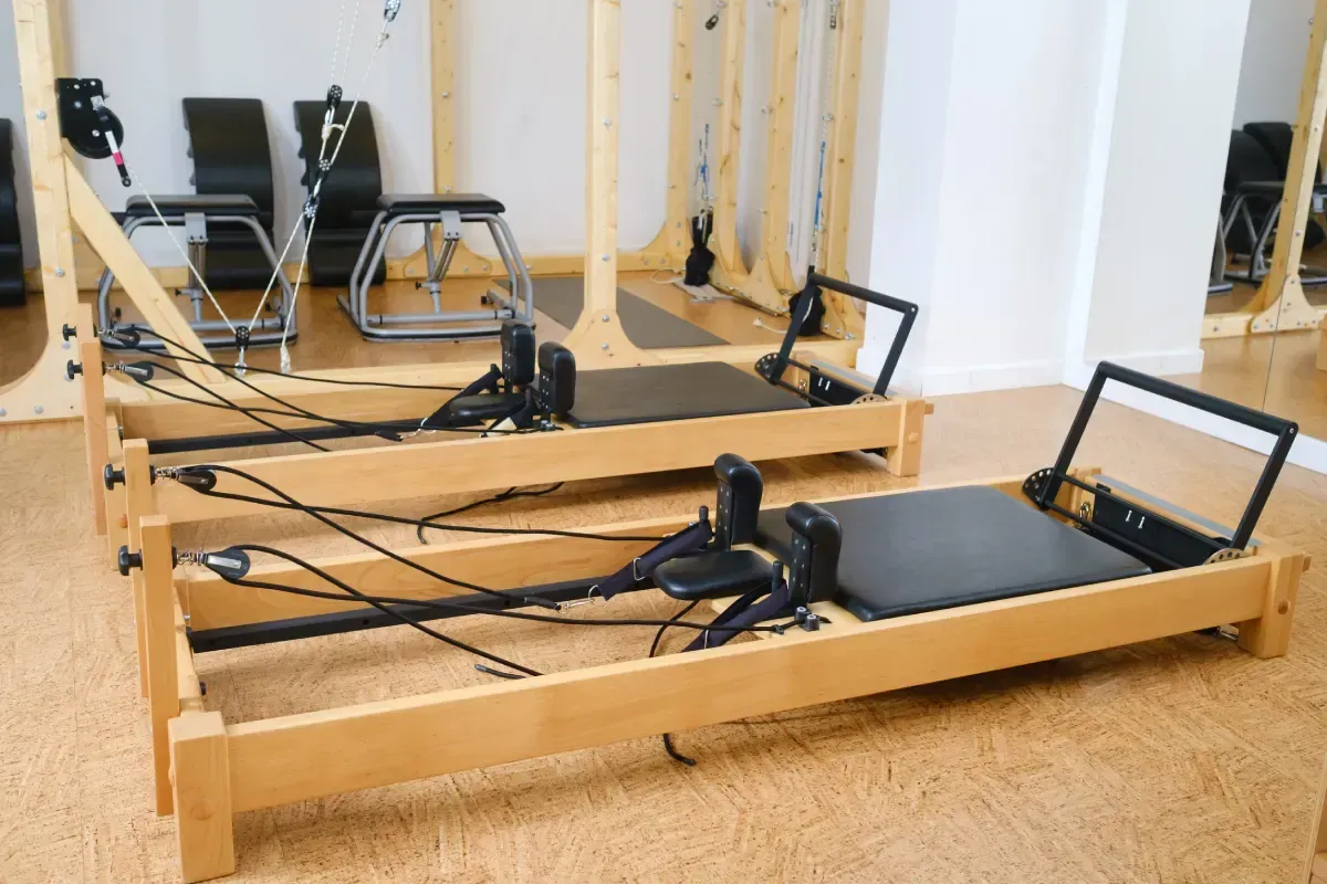 Dos reformers de Pilates en un estudio de madera clara. Se ven el acolchado y los cables negros.