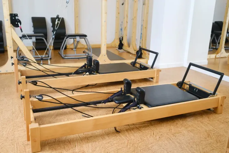 Dos reformers de Pilates en un estudio de madera clara. Se ven el acolchado y los cables negros.