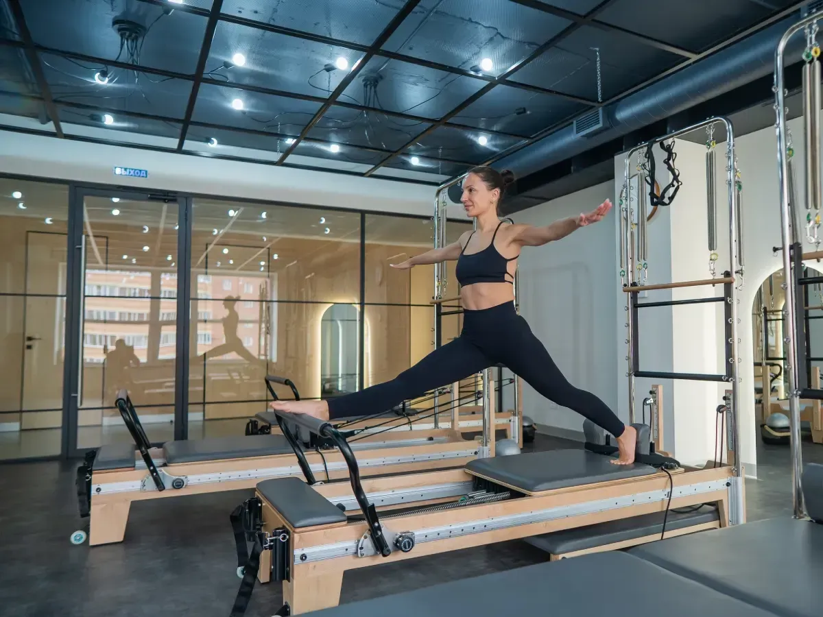 Mujer haciendo pilates en una máquina reformer, con las piernas separadas y los brazos extendidos