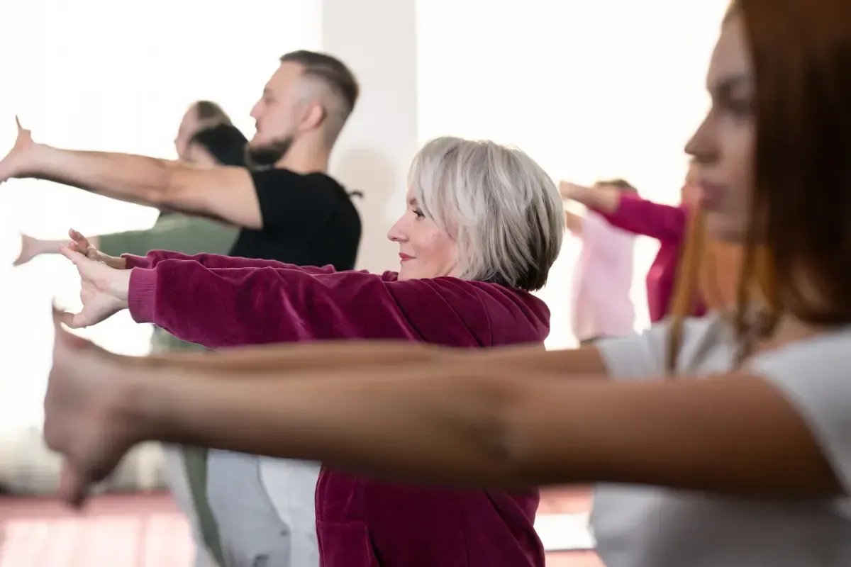Personas estirando los brazos hacia adelante en una clase de ejercicio grupal.