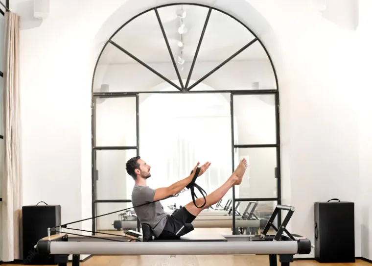 Hombre haciendo Pilates en un reformador, con una ventana arqueada al fondo.