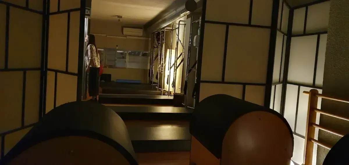 Un interior tenuemente iluminado con pasillo, escaleras y tabiques. Se ven dos objetos redondos en primer plano.