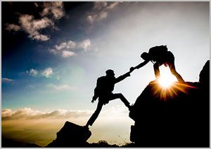 A man is helping another man climb a mountain.