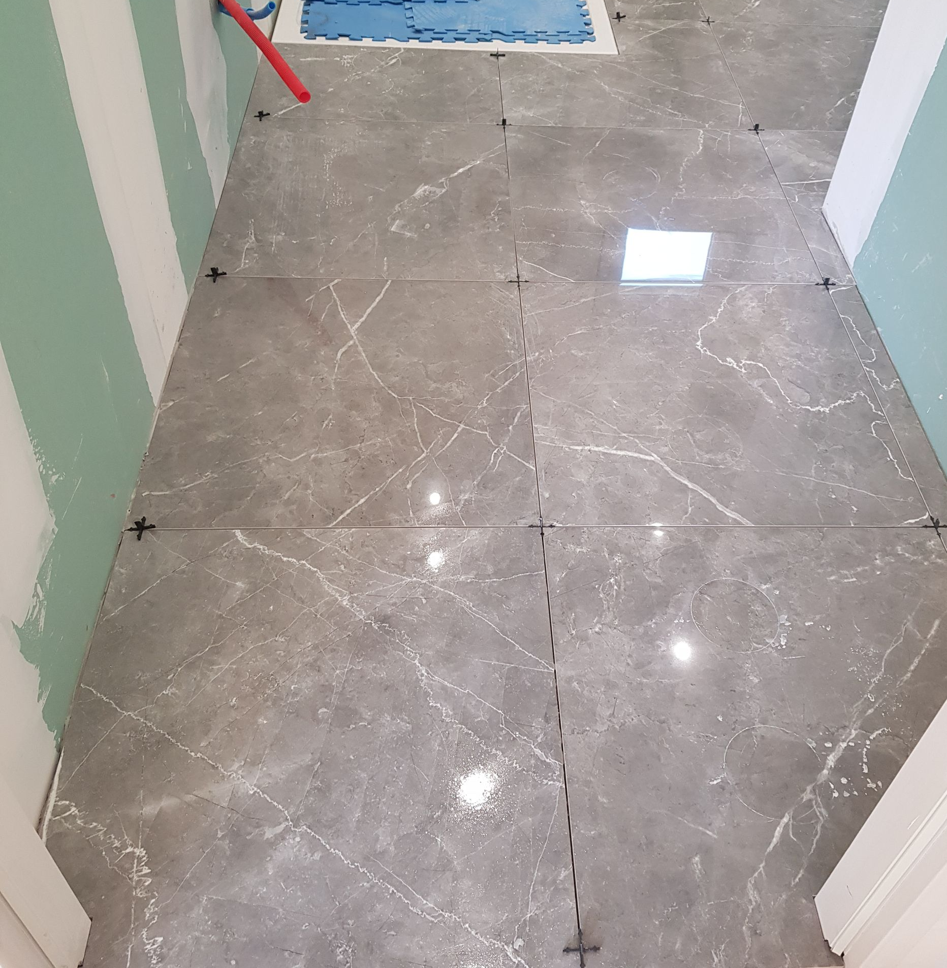 Carrelage aspect marbre gris posé au sol, avec des espaceurs entre les deux, dans une pièce aux murs verts et blancs.