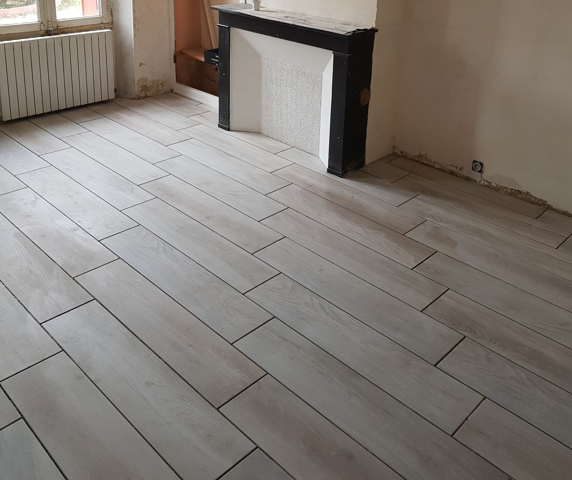 Carrelage aspect bois clair dans une pièce avec cheminée et radiateur.