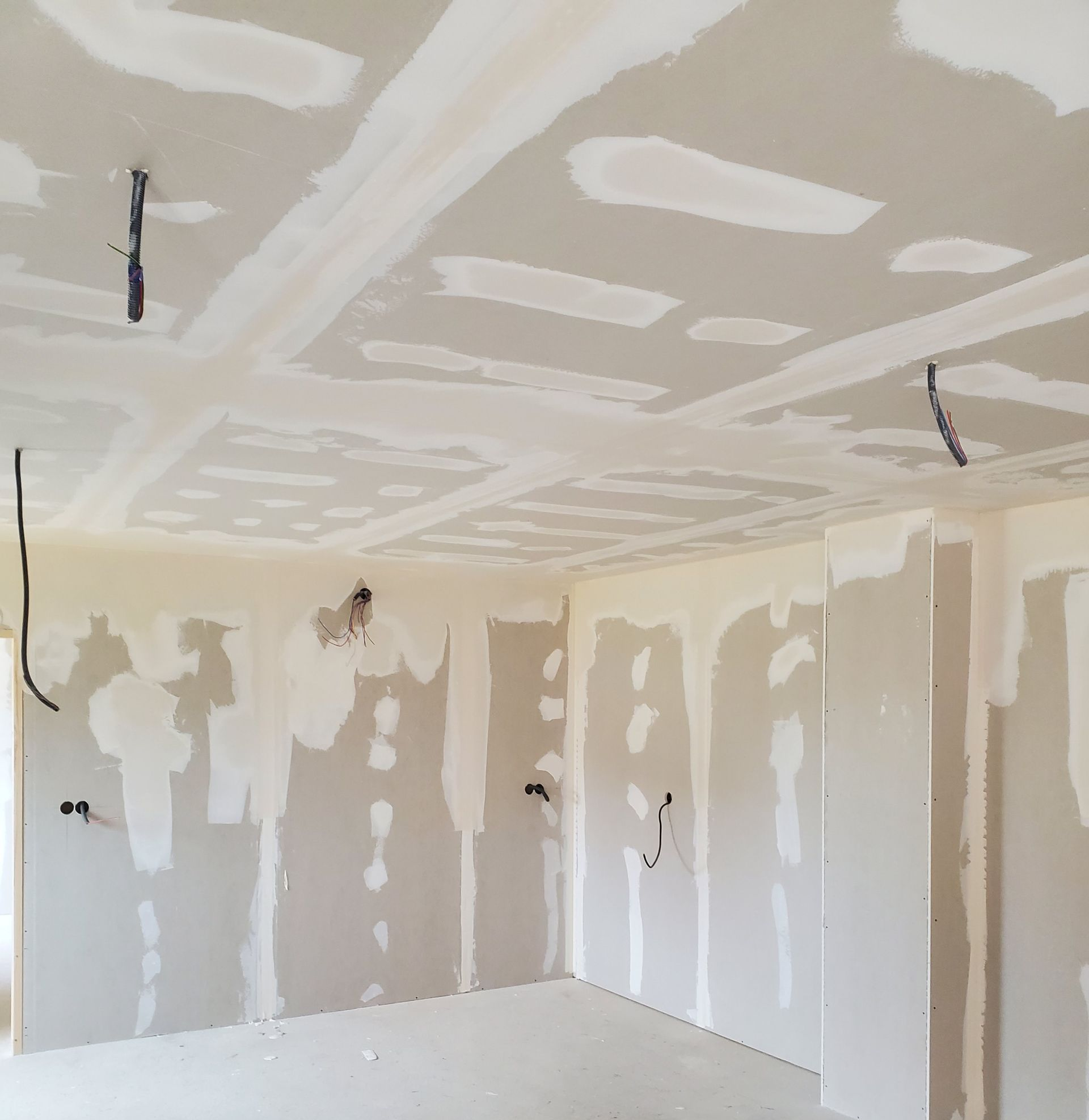 Pièce intérieure avec murs et plafond en plaques de plâtre non finis, joints collés et fils électriques.