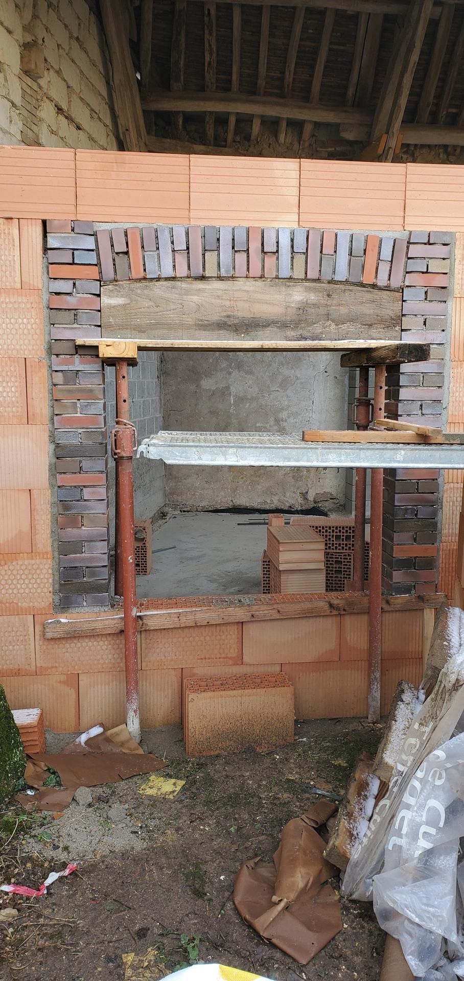 Travaux de maçonnerie en cours autour d'une ouverture de fenêtre. Un échafaudage soutient une poutre provisoire.