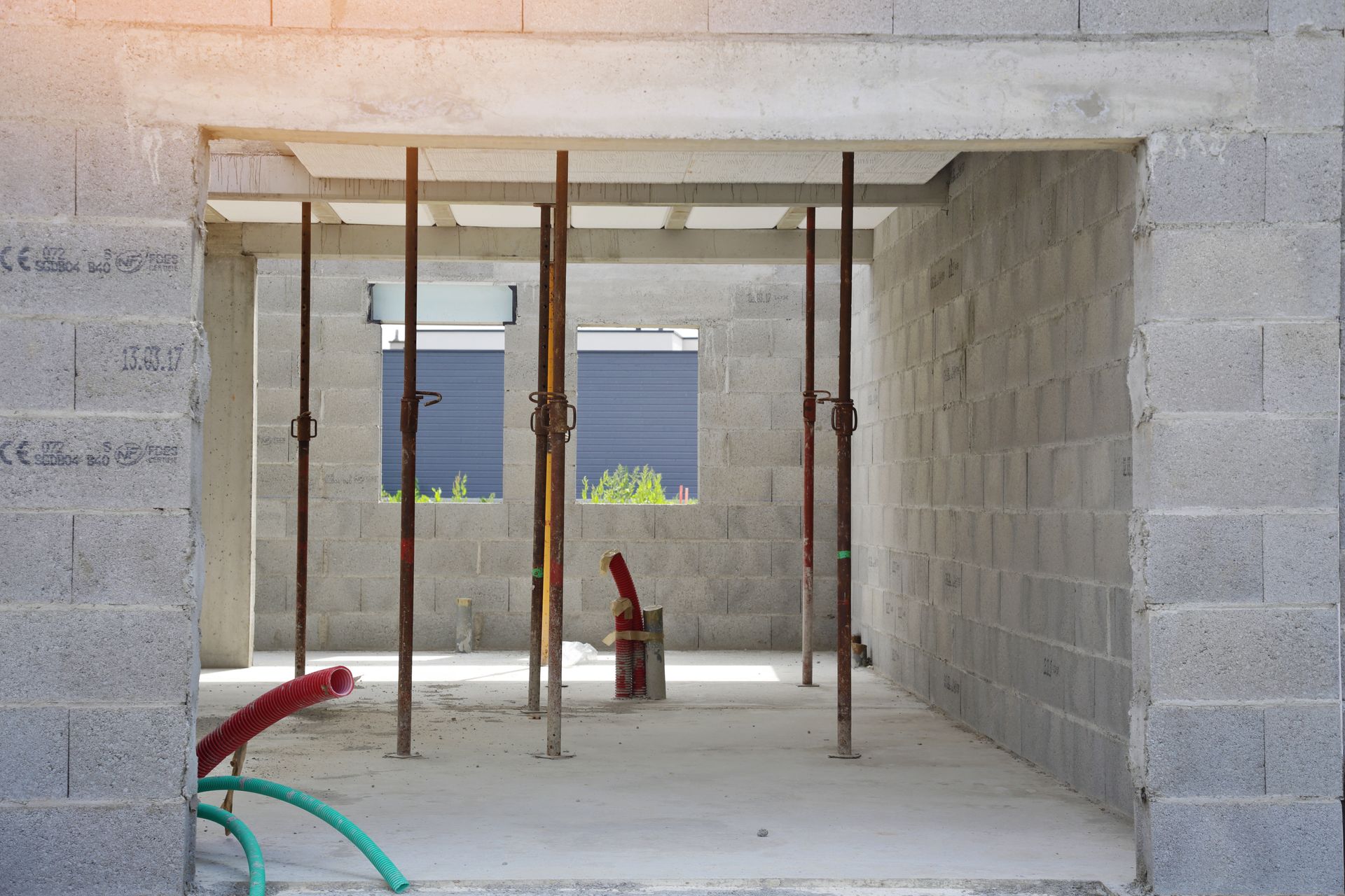 Intérieur d'un chantier de construction en blocs de béton, présentant des poutres de support et des ouvertures de fenêtres.