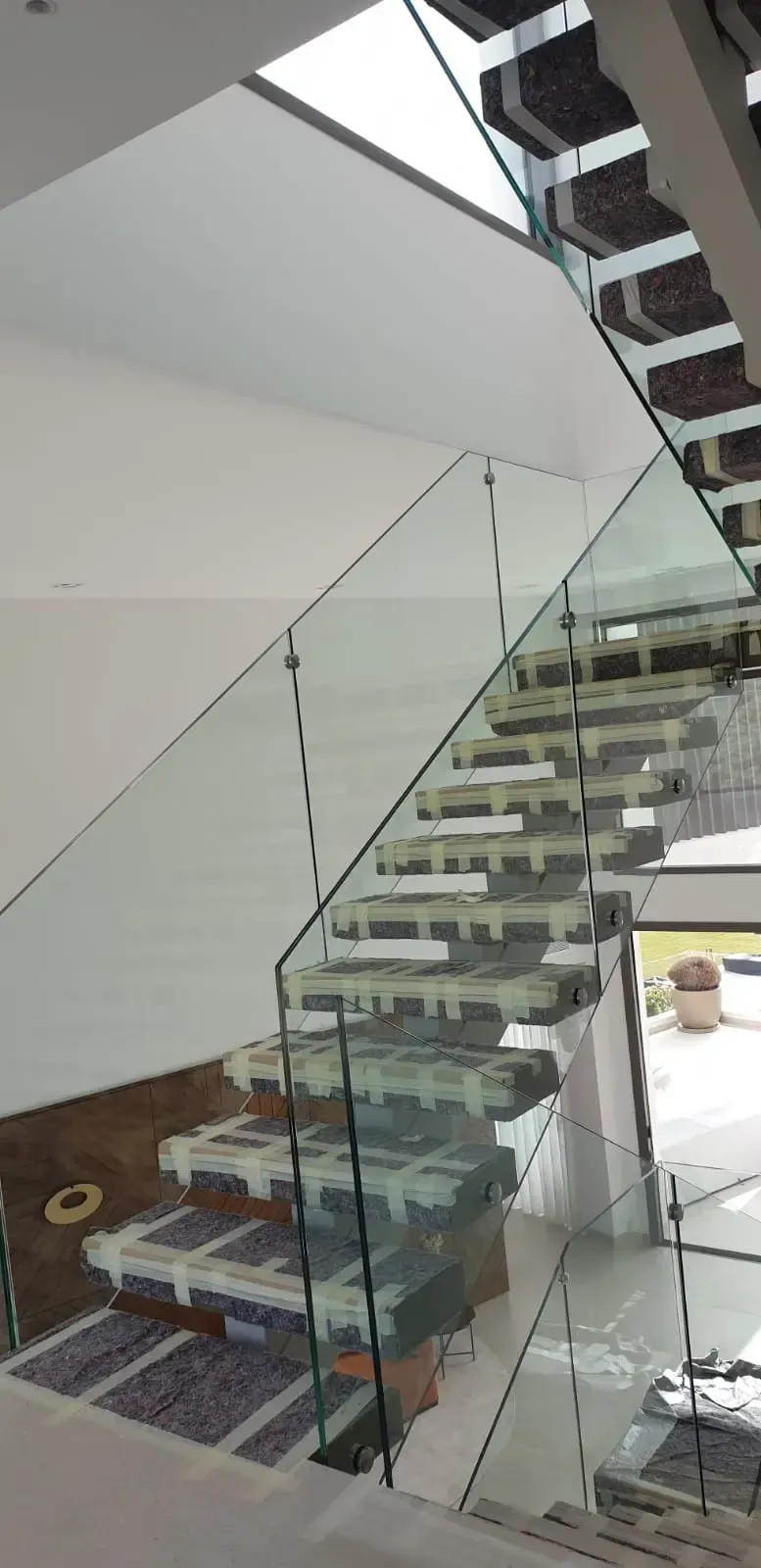Una escalera moderna con peldaños abiertos, barandillas de cristal y cubiertas de papel protector aún en los escalones.