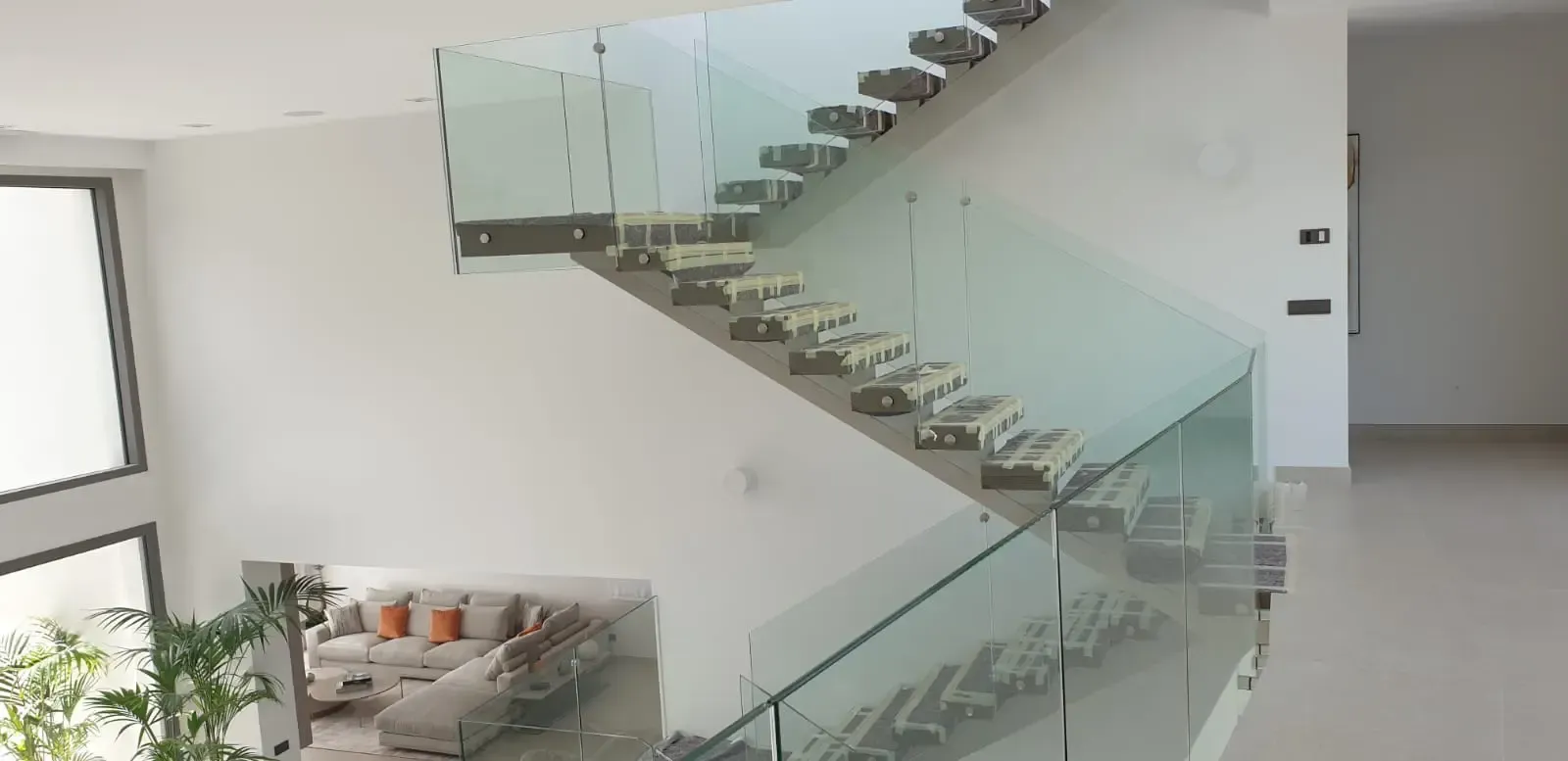 Un interior moderno con una escalera blanca con barandillas de cristal y pequeños vehículos de juguete colocados en cada escalón.
