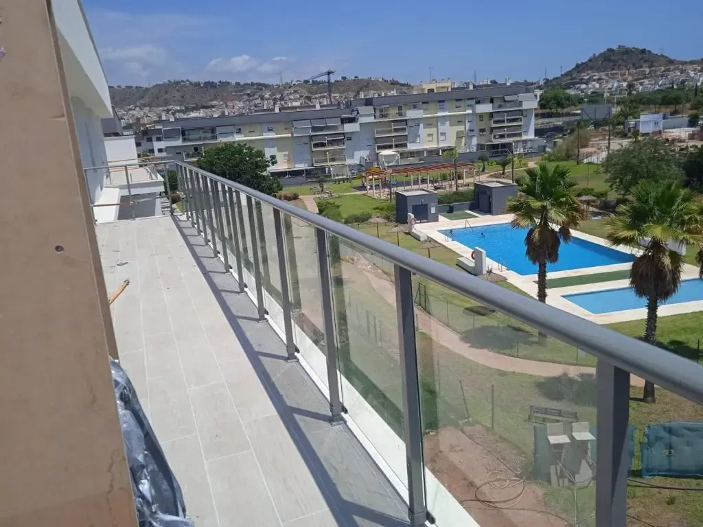Vista desde un balcón en picado que muestra el exterior de un edificio moderno con barandillas de cristal y vistas a una piscina azul.