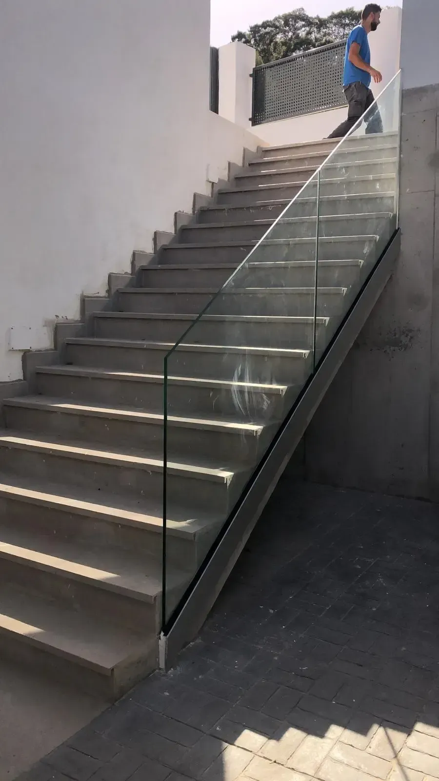 Una persona baja por una moderna escalera de hormigón con una barandilla de cristal entre dos paredes.