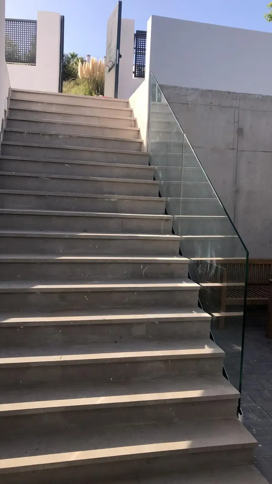 Una escalera de hormigón que conduce a una abertura, con una barandilla de cristal en el lado derecho.