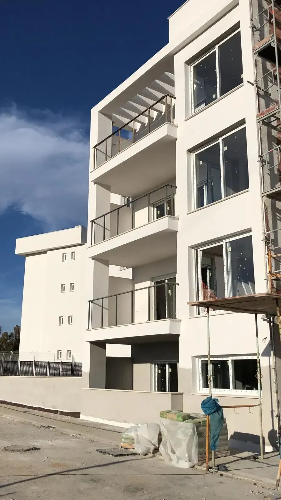 Un edificio de apartamentos blanco de reciente construcción bajo un cielo azul brillante, con balcones apilados y andamios exteriores.