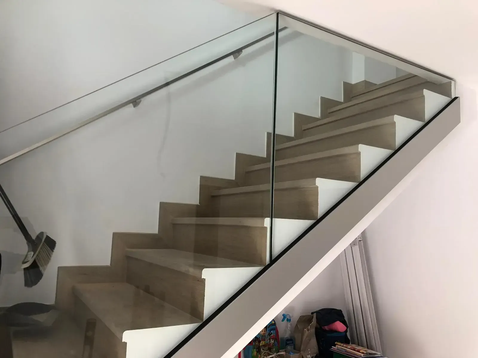 Escalera con peldaños de tonos claros y una barandilla moderna de cristal transparente con un pasamanos metálico fino.