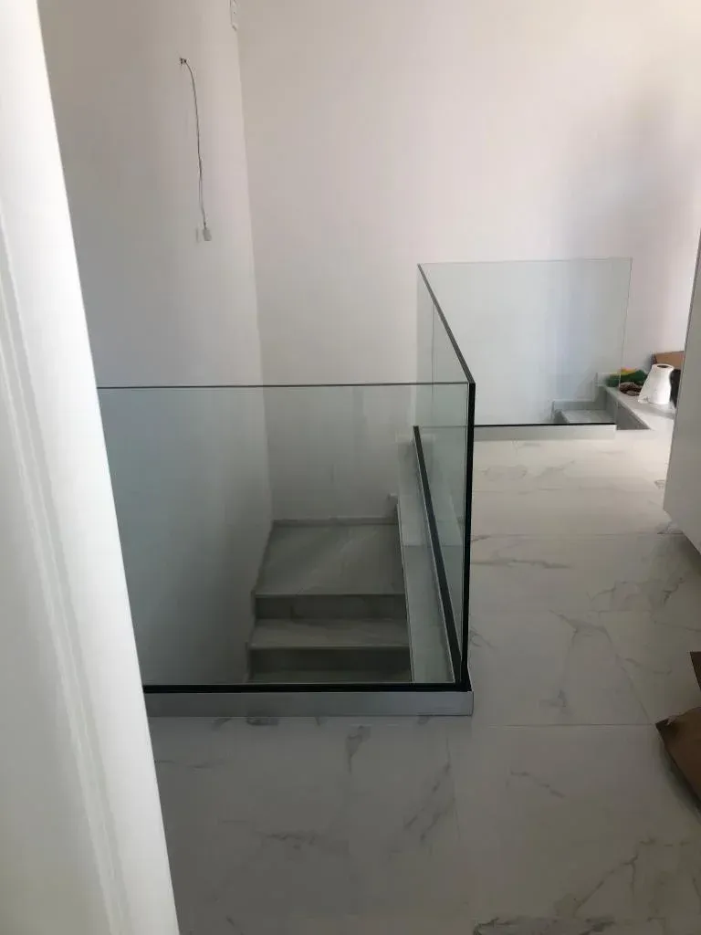 Una escalera con barandillas de cristal y suelo de imitación mármol en un interior minimalista blanco.