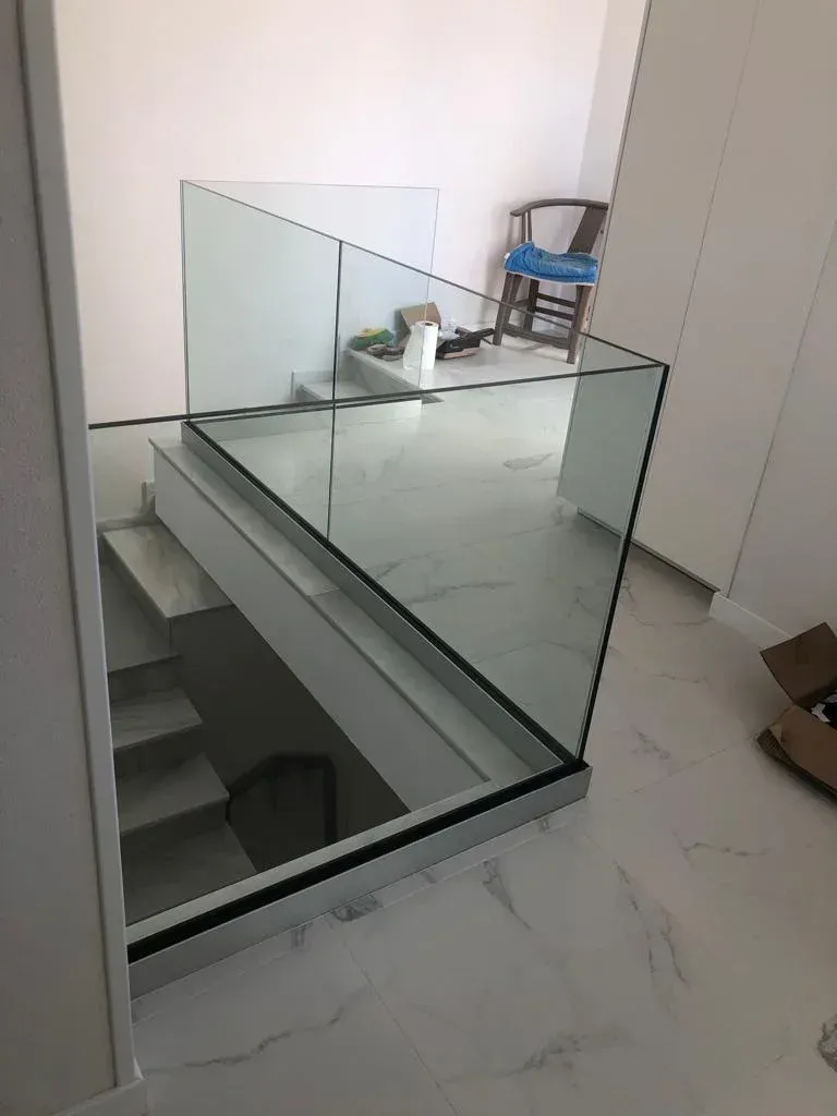 Escalera moderna con suelo de mármol claro y barandilla de cristal sin marco con vistas al rellano.